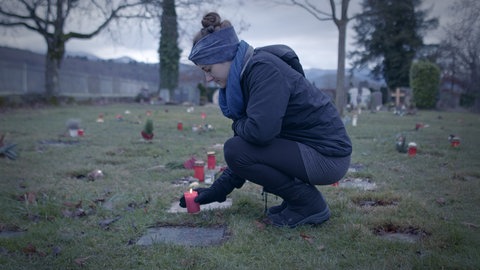 Eine Frau stellt eine Kerze an einem Grab auf einem Friedhof ab.