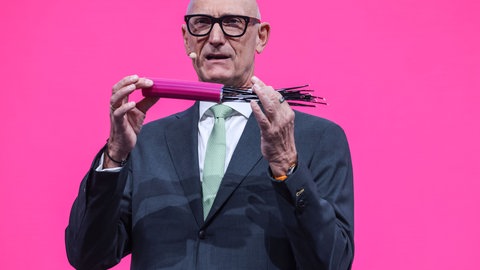 Timotheus Höttges, Vorstandsvorsitzender der Deutschen Telekom, spricht zu den Aktionären mit einem Glasfaser-Kabel in in der Hand. 