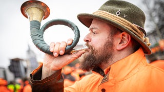 Ein Jäger nimmt an einer Demonstration gegen Jagdbeschränkungen teil und bläst dabei ein Jagdhorn.