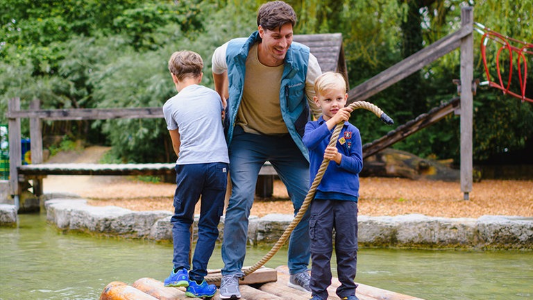 Eine Familie hangelt sich mit dem Floß über die "See" auf dem Spielplatz Wasserwelt der Insel Mainau.