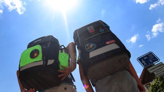 Zwei Kinder laufen mit ihren Schulranzen in der Sonne.