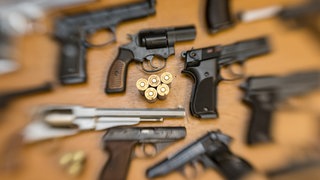 Pistolen und Revolver und Munition liegen auf einem Tisch in einer gesicherten Asservatenkammer (Symbolbild)