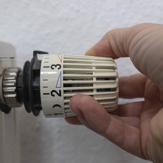 Eine Hand greift nach dem Thermostatkopf eines Heizkörpers, um die Temperatur einzustellen. In Baden-Württemberg und Rheinland-Pfalz waren die Haushalte im Januar relativ sparsam beim Heizen, zeigt eine Techem-Analyse.