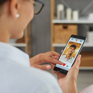 Frau sieht einen Mann auf einer Dating-App: Die Hälfte der unter 30-jähringen datet per App. Es lauern Kostenfallen per Abos. Vergleiche der Partnerbörsen lohnen sich -nicht nur am Valentinstag.