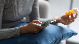 Eine Frau hält ein Handy in einer Hand und eine Pillendose in der anderen