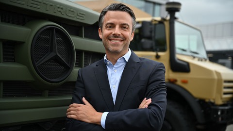 Dennis Kinzelmann steht vor einer militärischen Variante des Zetros und des Unimogs 4000 vor dem Daimler Truck-Werk in Wörth am Rhein.