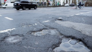 Autos fahren auf einer Straße mit Schlaglöcher: Den Städten und Gemeinden in Baden-Württemberg hat im vergangenen Jahr so viel Geld gefehlt wie noch nie: das Defizit lag bei 4,4 Milliarden Euro. In Rheinland-Pfalz betrug das Minus knapp 1,1 Milliarden. Die Angaben sind aus dem Kommunalen Finanzreport der Bertelsmann-Stiftung. 