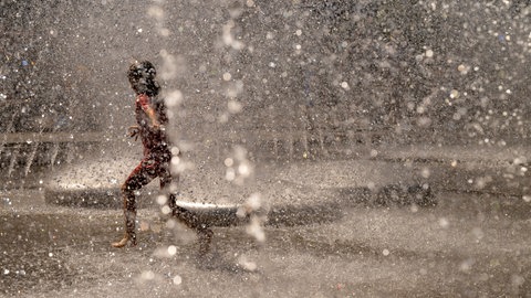 Ein Kind spielt bei heißem Wetter in einem Brunnen im Wasser.