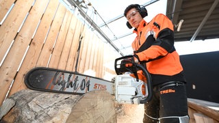 Im Stammwerk des Motorsägenherstellers Stihl sägt ein Arbeiter mit einer neu entwickelten Akku-Säge für den professionellen Einsatz einen Baumstamm durch. 