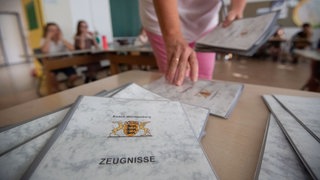 Eine Lehrerin einer Grundschule nimmt vor der Zeugnisausgabe Zeugnisse von einem Tisch. 
