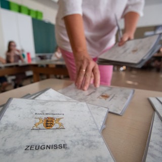 Eine Lehrerin einer Grundschule nimmt vor der Zeugnisausgabe Zeugnisse von einem Tisch. 