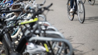 Eine Radfahrerin fährt in der Innenstadt an geparkten Fahrrädern vorbei. 