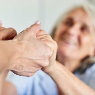 Die Hände einer Seniorin werden gehalten.