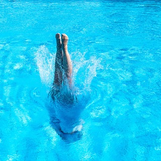 Eine Frau tauch mit einem Kopfsprung in ein Schwimmerbecken ein.