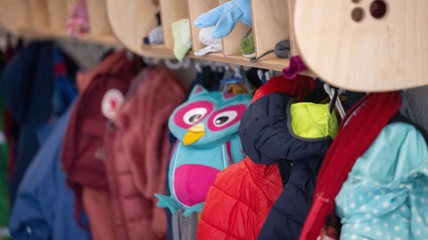 Jacken und Taschen hängen an einer Garderobe einer Kita. 