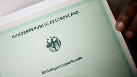 Ein Mann hält eine Einbürgerungsurkunde der Bundesrepublik Deutschland in der Hand. 