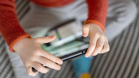 Ein Kleinkind sitzt auf einem Sofa und hält ein Tablet in den Händen.