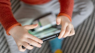 Ein Kleinkind sitzt auf einem Sofa und hält ein Tablet in den Händen.