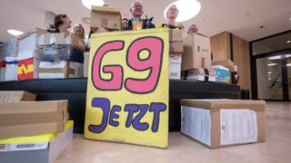 Unterstützer der Elterninitiative "G9 Jetzt! BW" stehen im Foyer des Bürger- und Medienzentrum des Landtags von Baden-Württemberg hinter Kartons, in denen sich Unterschriftenlisten befinden. 