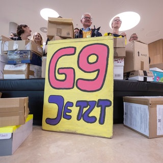 Unterstützer der Elterninitiative "G9 Jetzt! BW" stehen im Foyer des Bürger- und Medienzentrum des Landtags von Baden-Württemberg hinter Kartons, in denen sich Unterschriftenlisten befinden. 