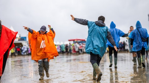 Besucher des Southside-Festival gehen in Gummistiefeln und Regenkleidung über das Festivalgelände. 