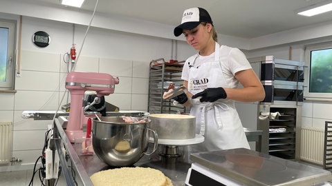 Bäckerin steht in der Backstube und arbeitet an einer Torte.
