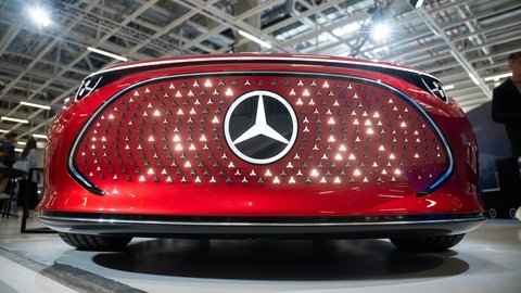 Ein Elektroauto mit leuchtendem Mercedes-Stern steht in einer Halle des Mercedes Benz eCampus.