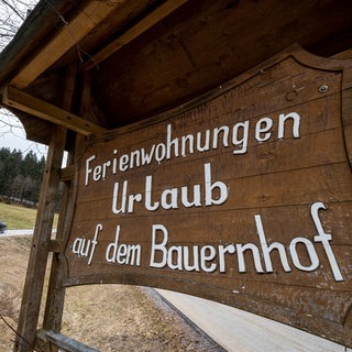 "Ferienwohnungen Urlaub auf dem Bauernhof" steht auf einem Schild an einer Straße.