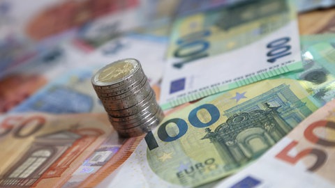 Ein Stapel mit Zwei-Euro-Münzen steht auf verschiedenen Euro-Banknoten. Baden-Württemberg muss in den kommenden Jahren mit weniger Steuereinnahmen auskommen als ursprünglich geplant.