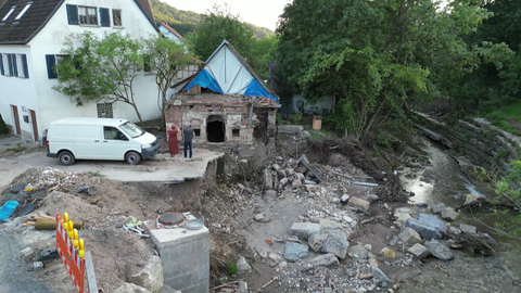 Michaela und Joachim Knödler schauen auf den zerstörten Schuppen und stehen auf dem vom Bach weggespülten Hof.