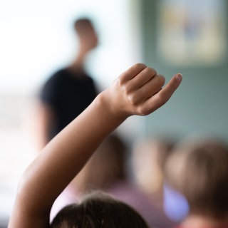 Schülerinnen und Schüler einer vierten Klasse einer Grundschule nehmen am Unterricht teil, eine Schülerin meldet sich (Archivbild).