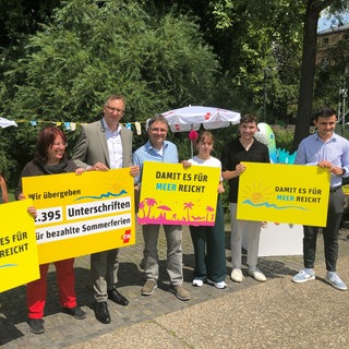 Beim GEW-Protest werden Plakate gegen die Sommerferien-Arbeitslosigkeit von Lehrkräften im Referendariat hochgehalten.