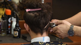 In einem Barbershop werden einem Kunden die Haare geschnitten.