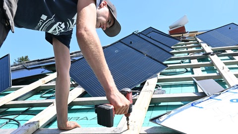 Ein Handwerker arbeitet bei der Montage eine Solaranlage auf einem Dach (Symbolbild).