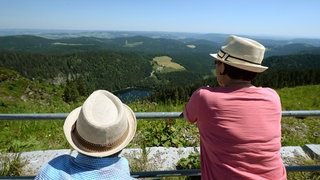 Zwei Touristen mit Strohhüten betrachten auf dem Gipfel des Feldbergs im Schwarzwald das Panorama. 2024 haben die Gäste- und Übernachtungszahlen in Baden-Württemberg weiter zugenommen.
