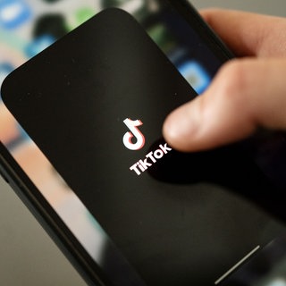 Ein Teenager tippt auf das TikTok-Logo auf einem Smartphone (Symbolbild).