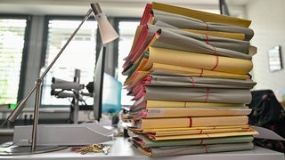 Ein Stapel mit Akten liegt auf einem Schreibtisch in einem Behördenbüro