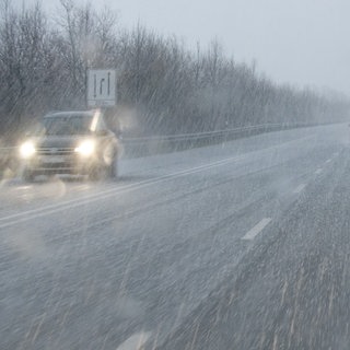 Autos fahren während eines Gewitters mit Graupel auf einer mit Graupelkörnern bedeckten Straße.