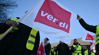 Mitarbeiter eines privaten Busunternehmens stehen mit Fahnen der Dienstleistungsgewerkschaft Verdi bei einem Warnstreik vor dem Unternehmen. 
