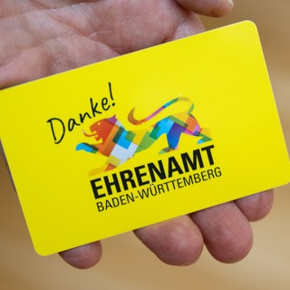 Eine Person hält die Ehrenamtskarte bei der Vorstellung auf der Pressekonferenz in die Kamera.