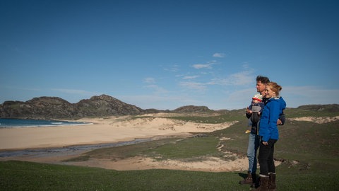 Familie steht am Strand auf der Insel Colonsay und schaut auf das Meer.