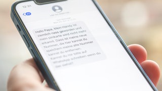 Eine Frau hält ein Smartphone in ihrer Hand, auf dessen Display eine Betrugs-SMS zu lesen ist.