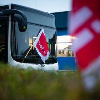 Eine ver.di-Fahne hängt an einem geparkten Linienbus. Beschäftige im privaten Busgewerbe streiken in Baden-Württemberg (Symbolbild).