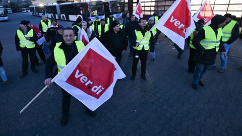 Mitarbeiter eines privaten Busunternehmens stehen mit Fahnen der Dienstleistungsgewerkschaft Verdi bei einem Warnstreik vor dem Unternehmen.