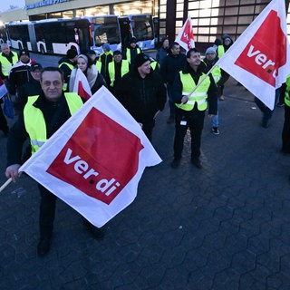 Mitarbeiter eines privaten Busunternehmens stehen mit Fahnen der Dienstleistungsgewerkschaft Verdi bei einem Warnstreik vor dem Unternehmen.