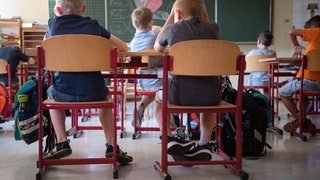Schülerinnen und Schüler sitzen in einer Grundschule in einem Klassenraum.