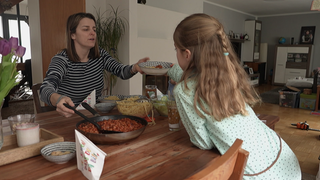 Eine Frau in gestriftem Oberteil reicht einem Mädchen im gepunkteten Kleid einen Teller mit Nudeln und Soße. Vera Maurer sagt, sie habe früher nicht geglaubt, dass sie einmal ein Leben als Hausfrau und Mutter führen würde.