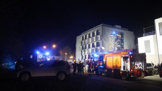 Ein Feuerwehrauto und ein Rettungswagen stehen vor einem Wohnblock in Neu-Ulm, nachdem es dort gebrannt hat. Mehrere Personen wurden verletzt, der Schaden liegt wohl im hohen fünfstelligen Bereich.
