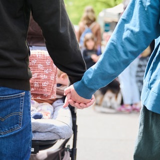 Eltern halten Händchen, während sie mit ihrem Baby im Kinderwagen über einen Markt gehen.