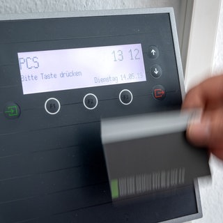 Symbolbild | Eine Hand fährt mit Bewegungsunschärfe an einem Gerät zur digitalen Zeiterfassung entlang: Ein Mitarbeiter erfasst seine Arbeitszeit digital an einem Terminal. 